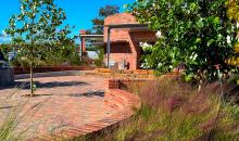 Red brick walkway leads to low circular building, with trees and grasses throughout the area.